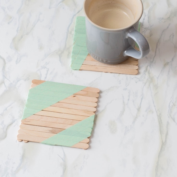 Two popsicle stick coasters with diagonal green washi tape stripes.