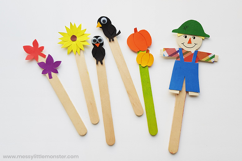 Paper stick puppets including a scarecrow, pumpkins, black birds, a sunflower, and leaves.