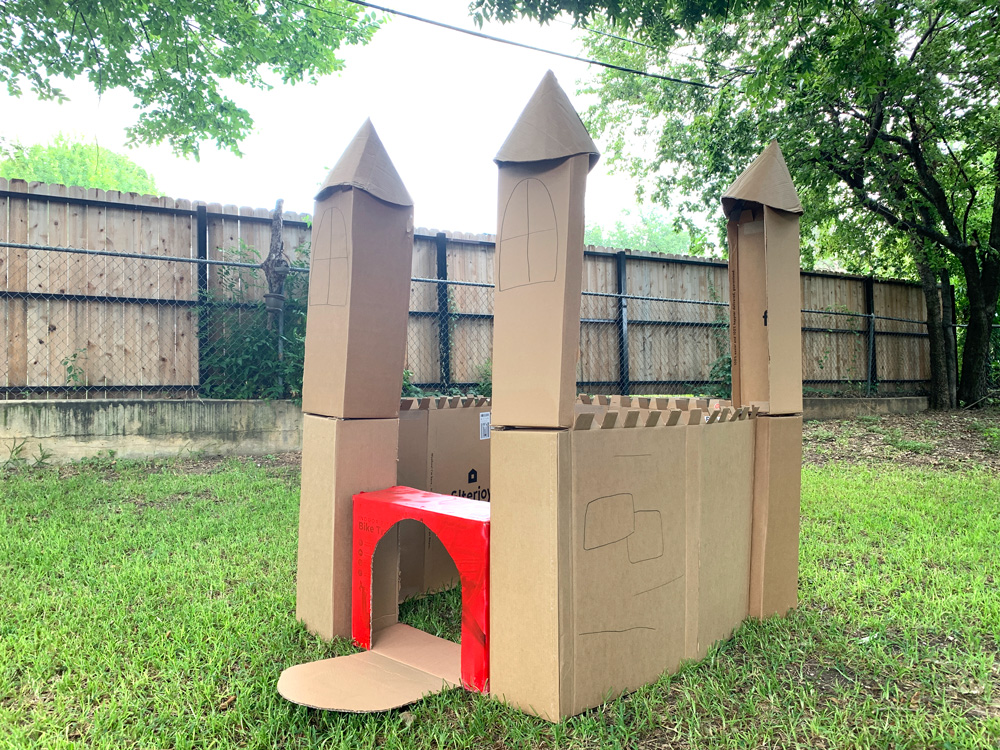 A cardboard fort with 4 towers on the corners, crenelated walls, and a drawbridge door.