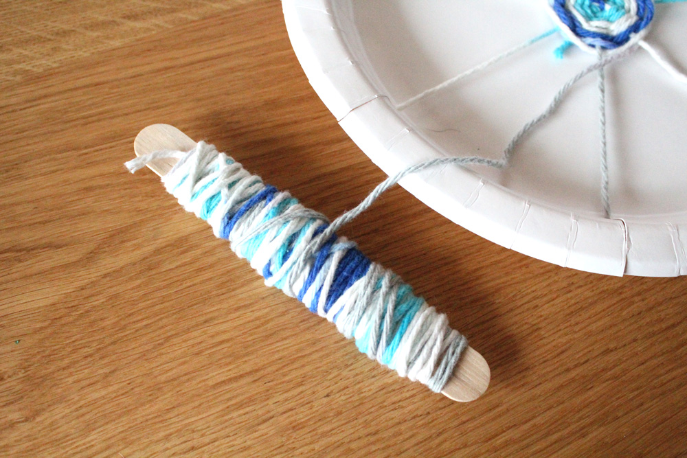 Blue yarn wrapped around a craft stick to use as a weaving shuttle.