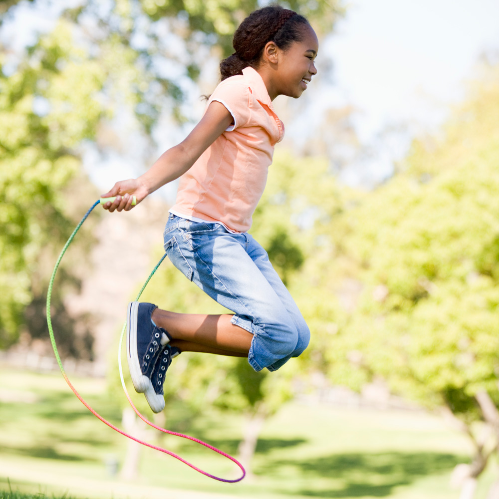 A child is mid-air with a jump rope outdoors.