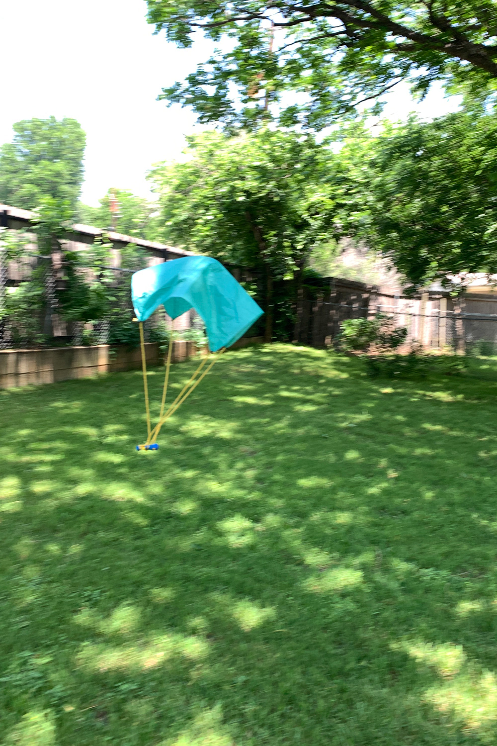 Tissue paper parachute carrying a minifigure through the air in a backyard.