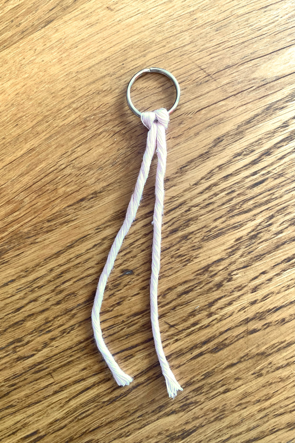 Pink macrame cord tied in the center to a metal keyring.