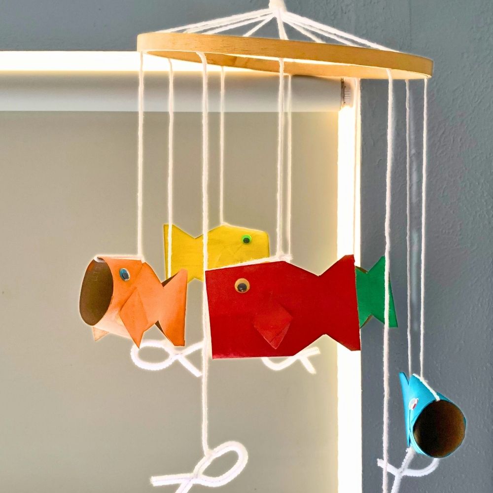 Ocean mobile with paper fish painted red, orange, yellow, green, and blue hanging from white yarn on a wood hoop.
