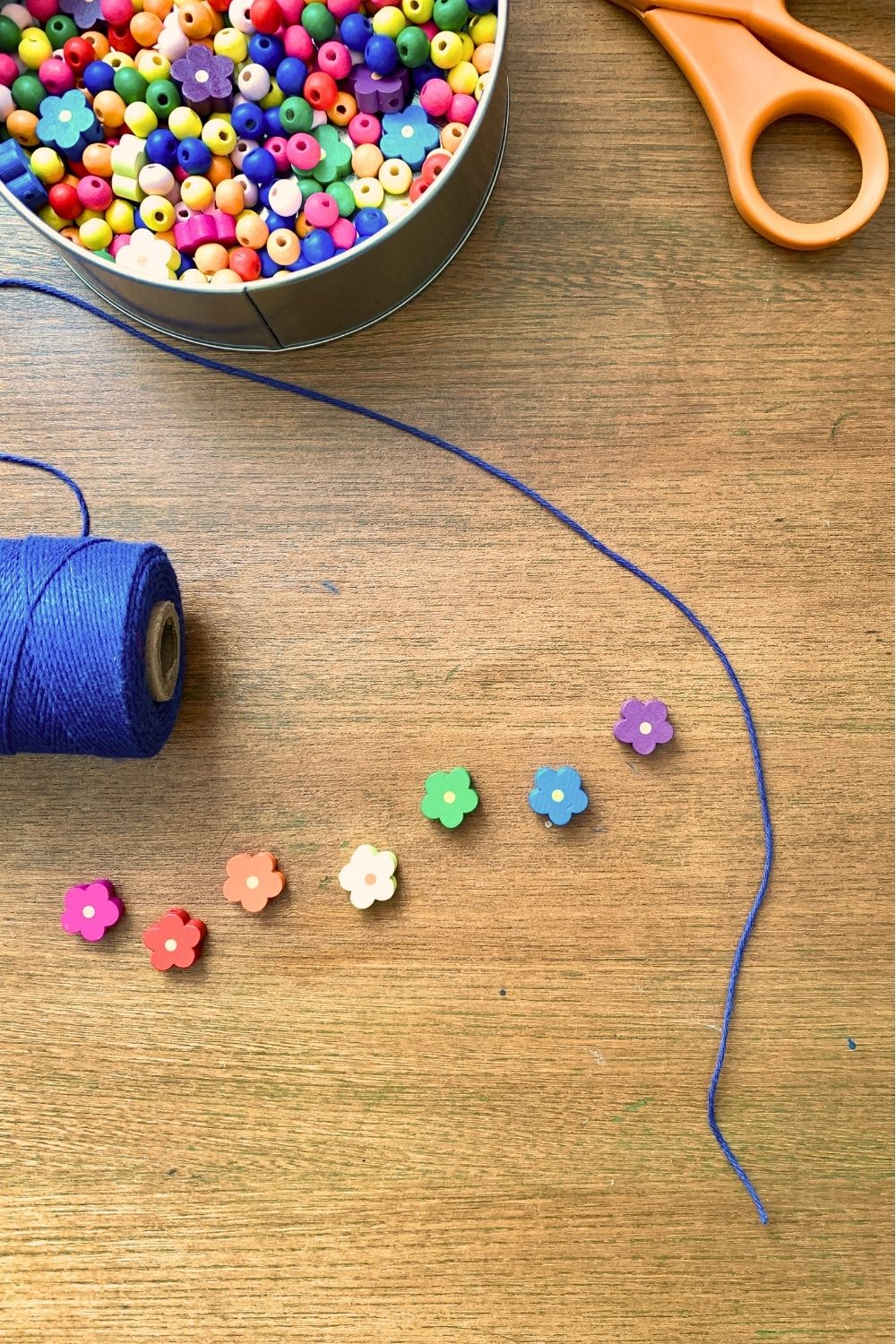 A long, blue cord beside flower beads laid in rainbow order from pink to purple.