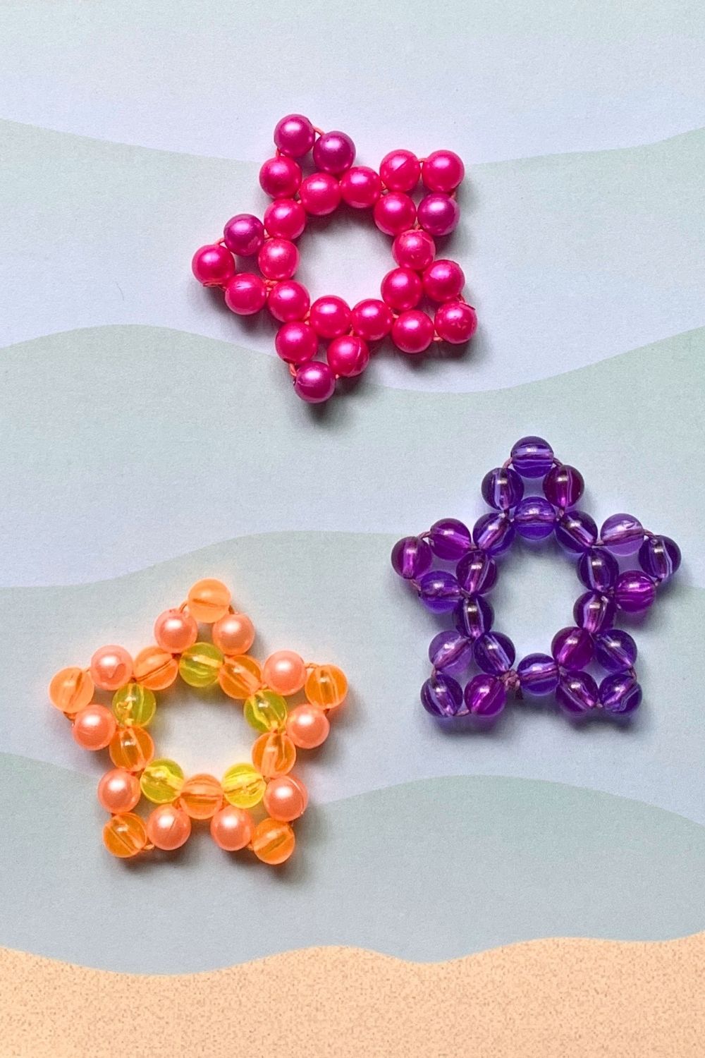 3 bead starfish in pink, purple, and orange beads on a paper beach background.