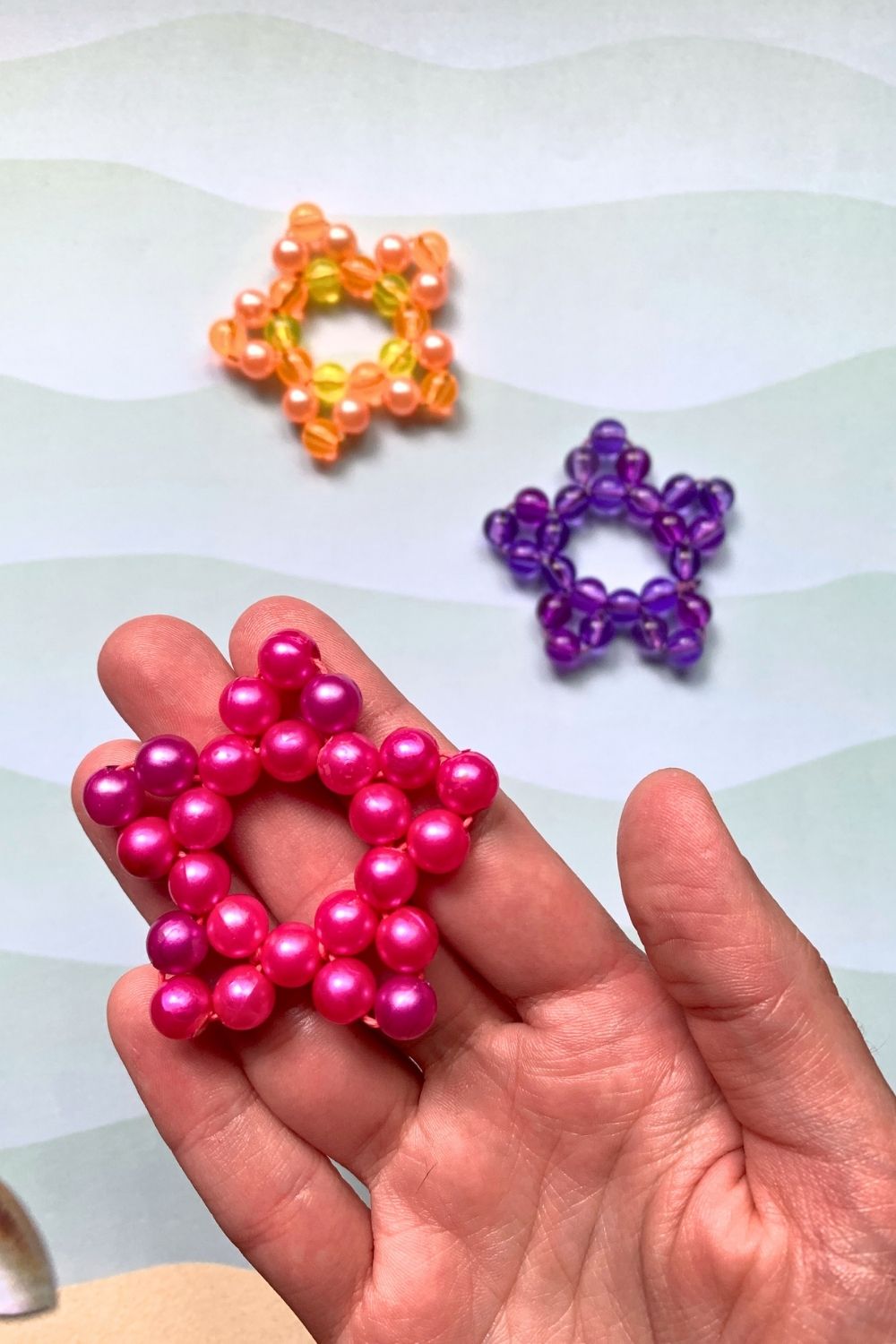A hand holding a pink bead starfish craft with orange and purple ones in the background.