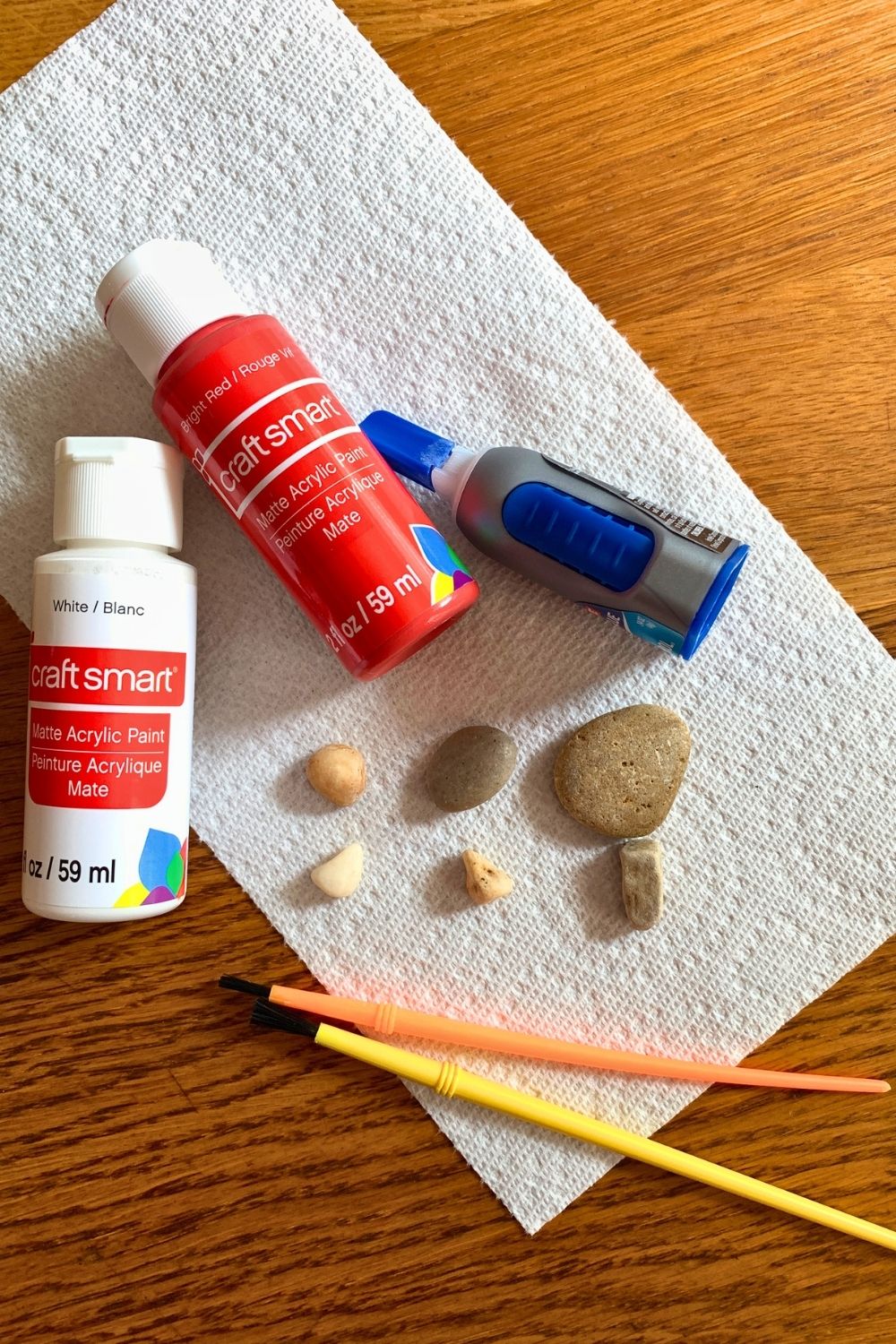 Bottles of white and red paint, super glue, paintbrushes, and small rocks.