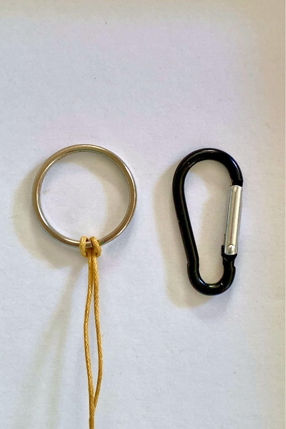 A round keyring looped with cord beside a carabiner-style one.