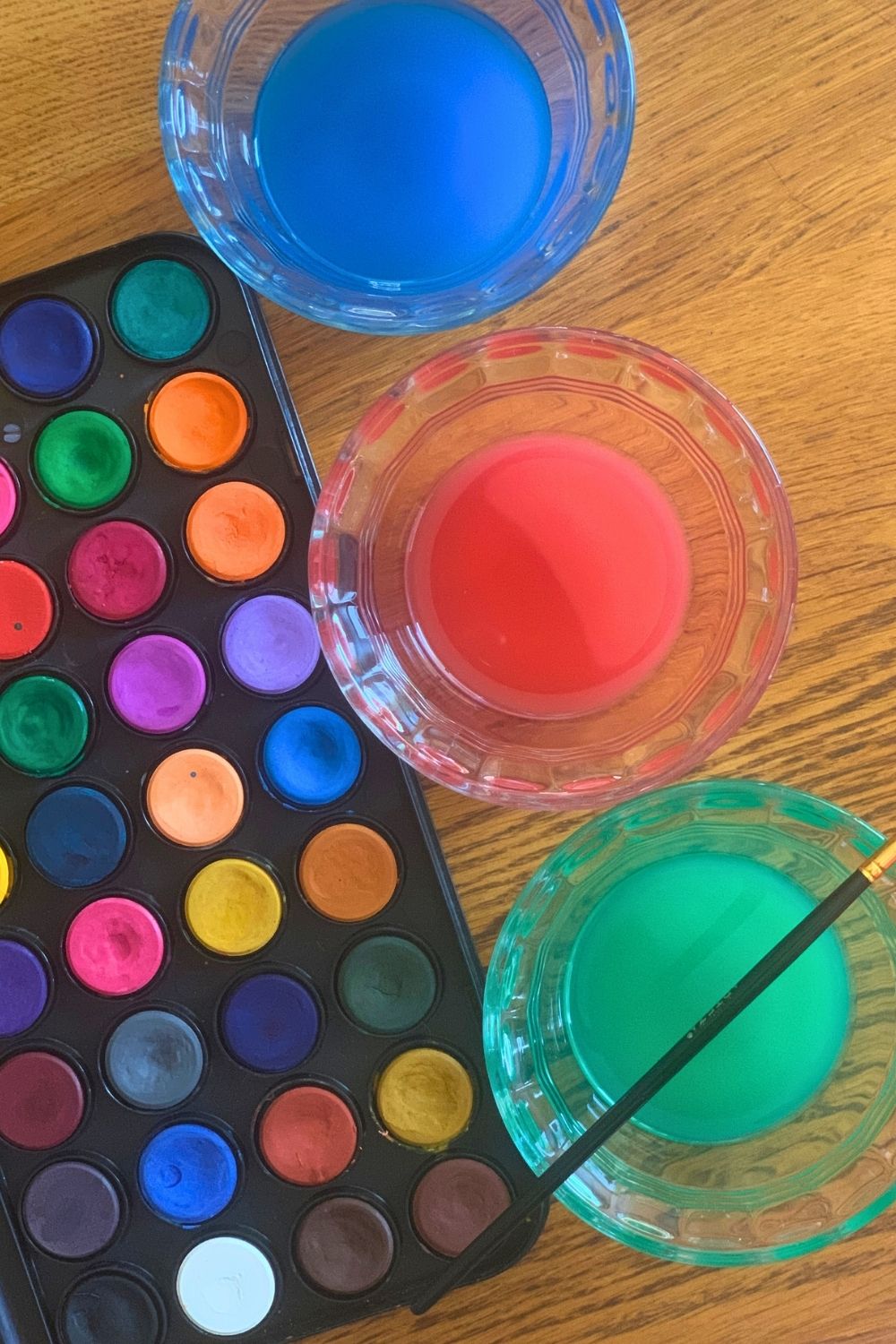 A watercolor palette beside 3 cups of colored water in blue, red, and green.