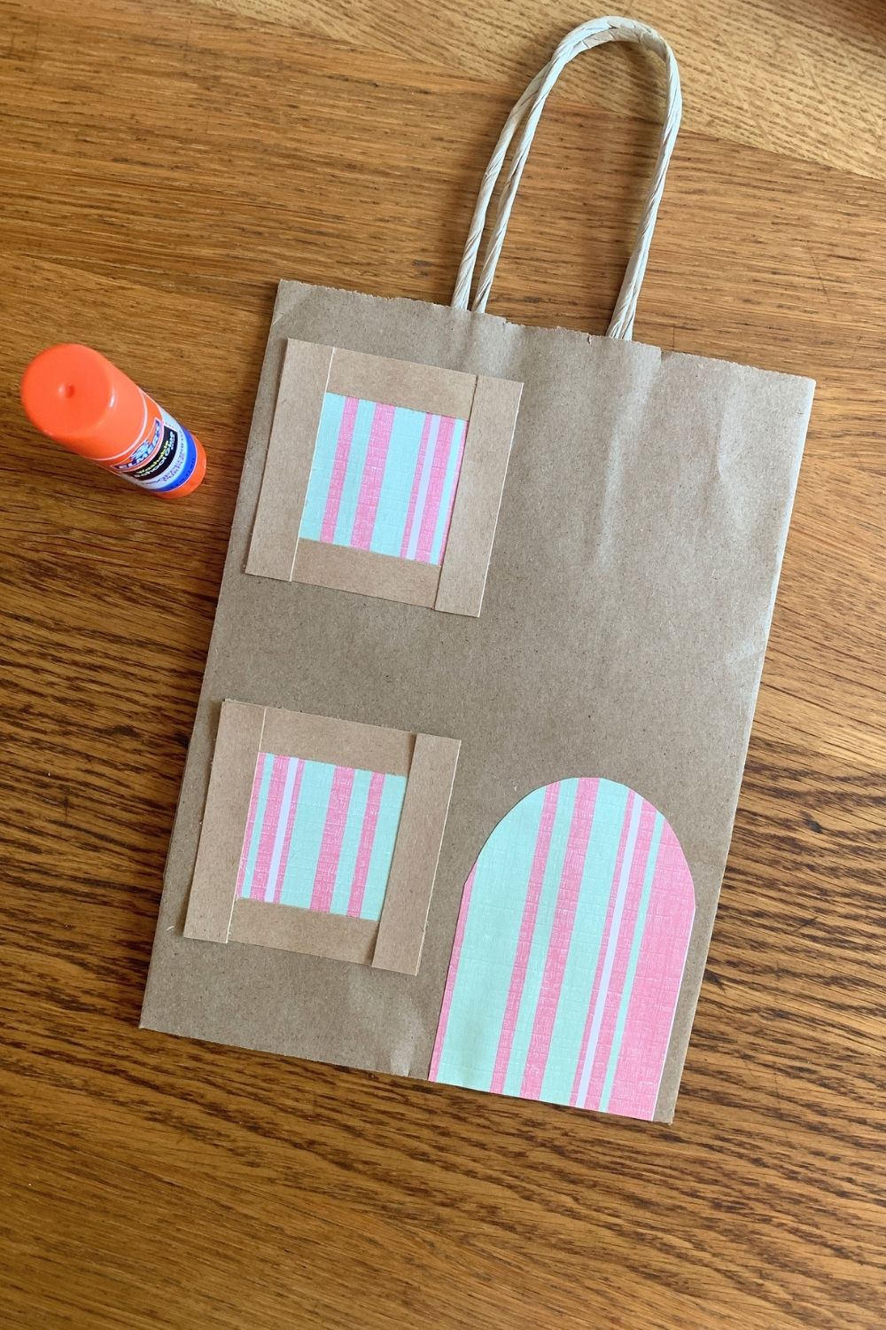 Gluing paper door and window shapes onto one side of the paper bag.