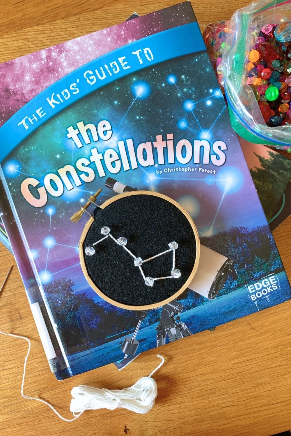 A big dipper constellation embroidery hoop on top of a book called The Kids' Guide to the constellations by Christopher Forest.