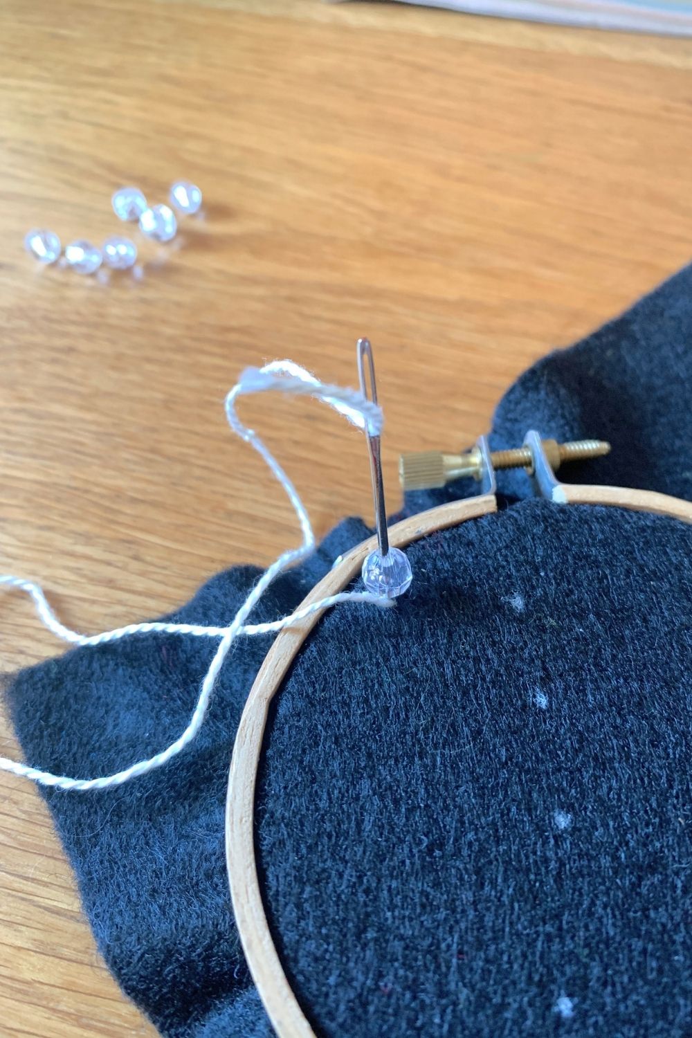 A clear plastic bead stitched onto black fabric with white thread.