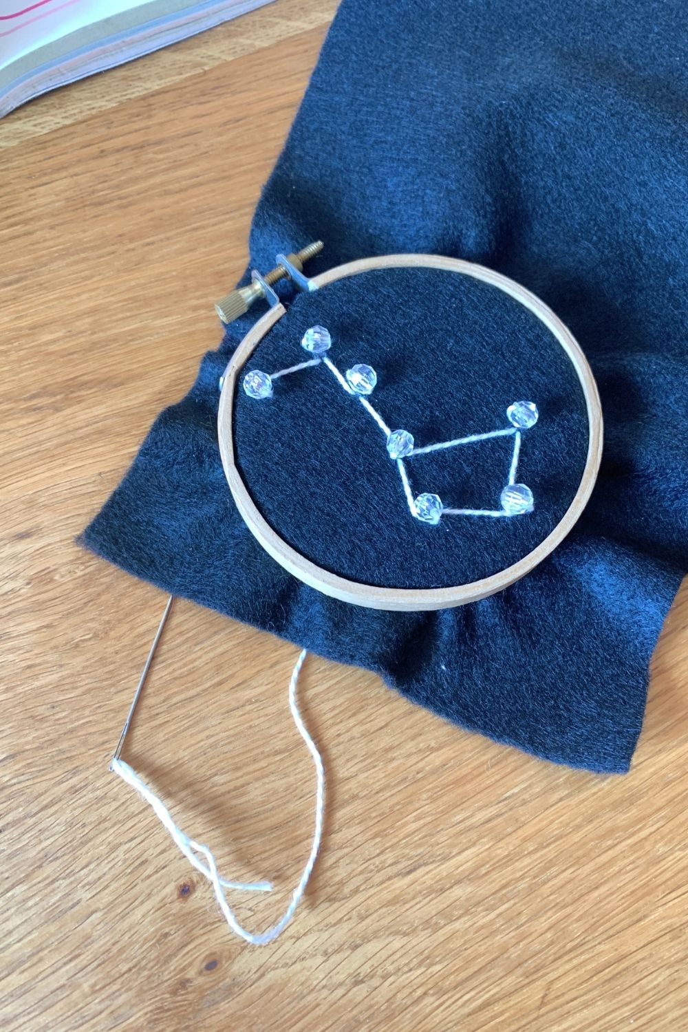 The big dipper in clear beads and white thread on a black felt background.