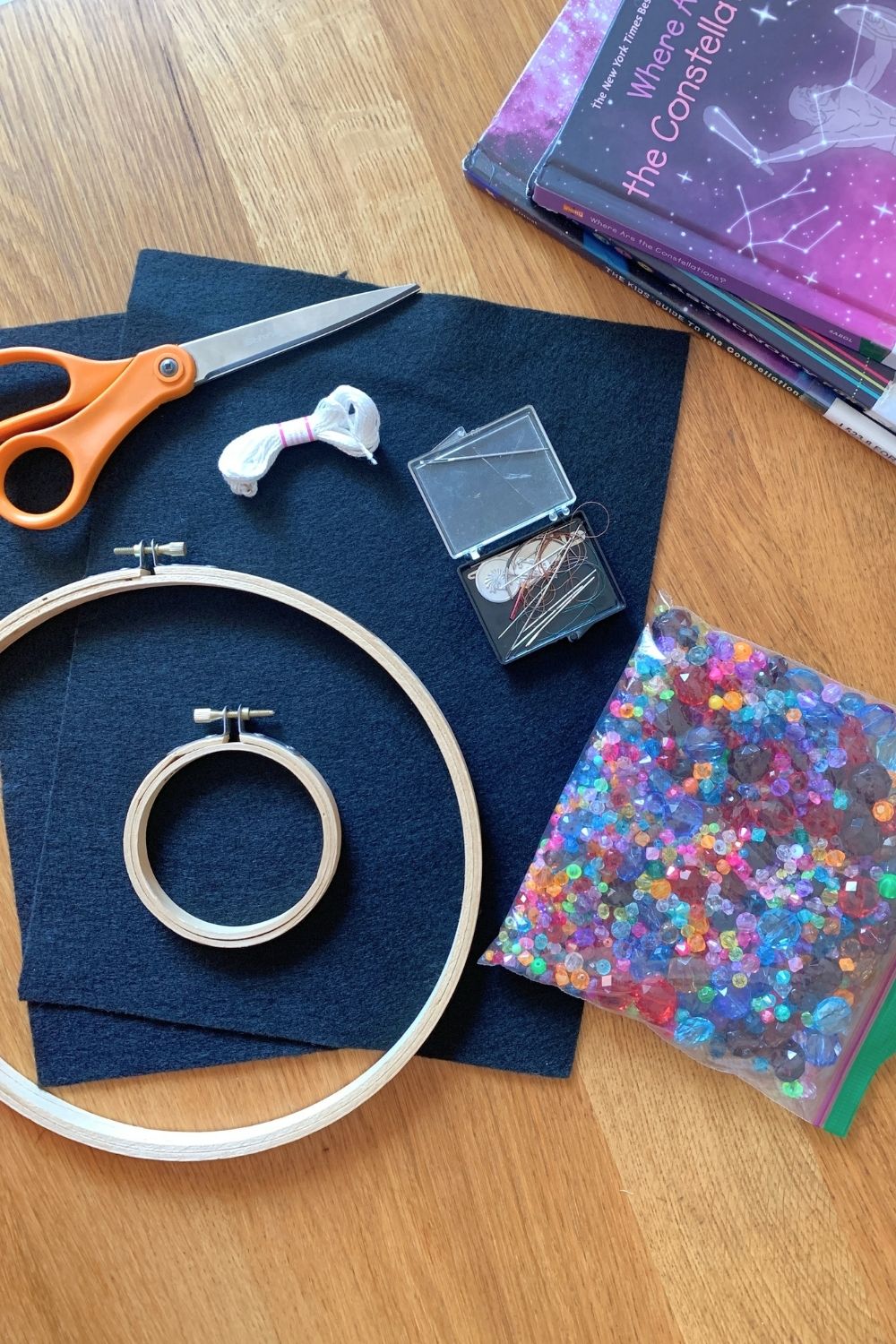 Black felt, sparkly plastic beads, 2 embroidery hoops, white thread, scissors, and a box of sewing needles.