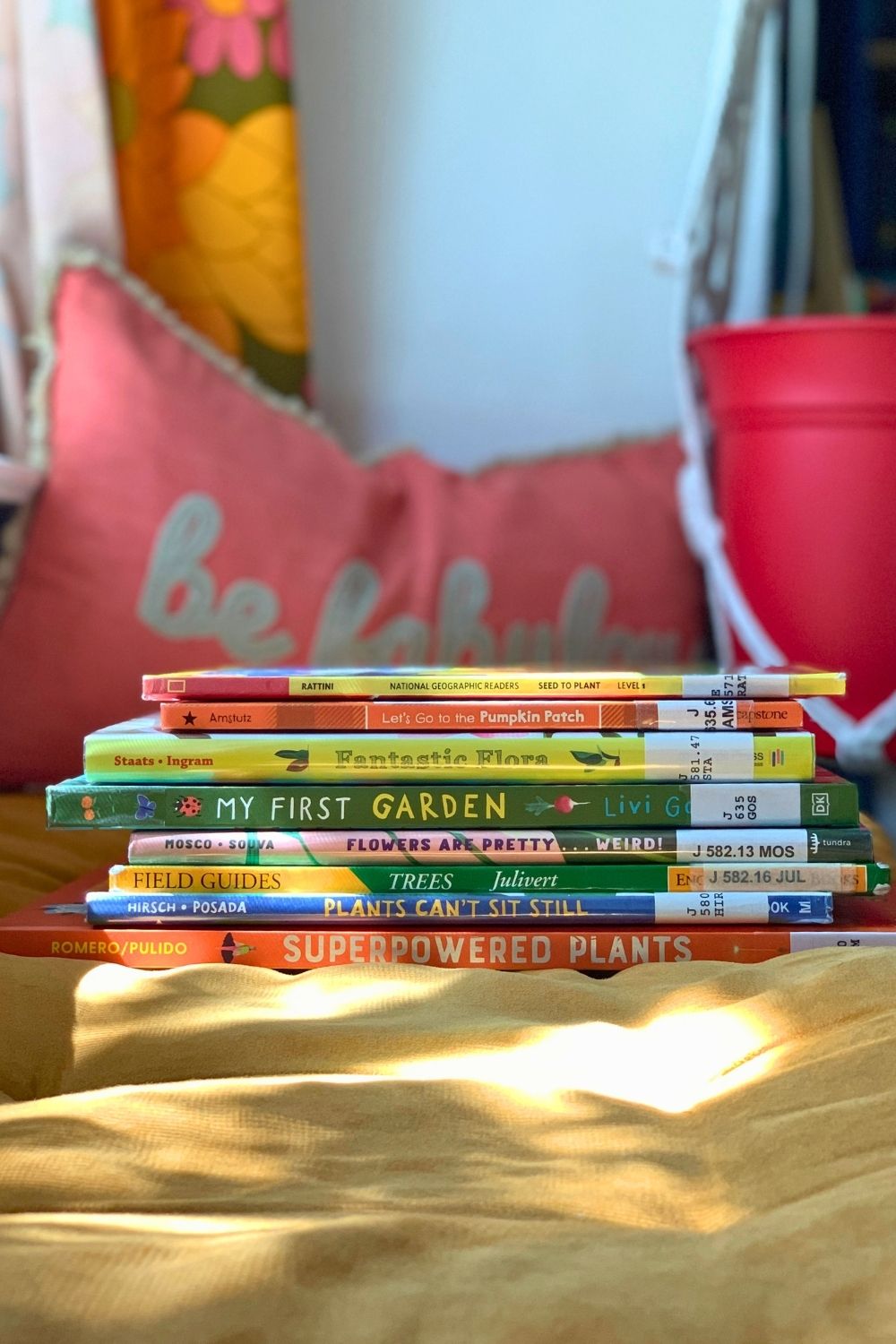 A stack of thin hardcover kids' books in a sunny window seat.