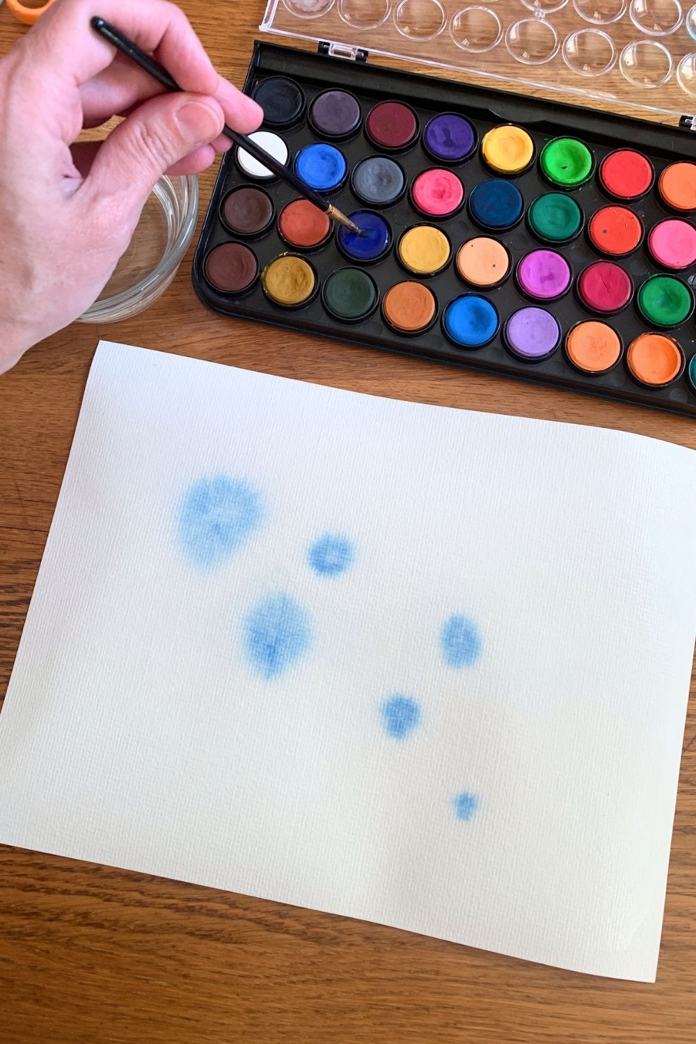 Brushing blue watercolor blobs on paper.