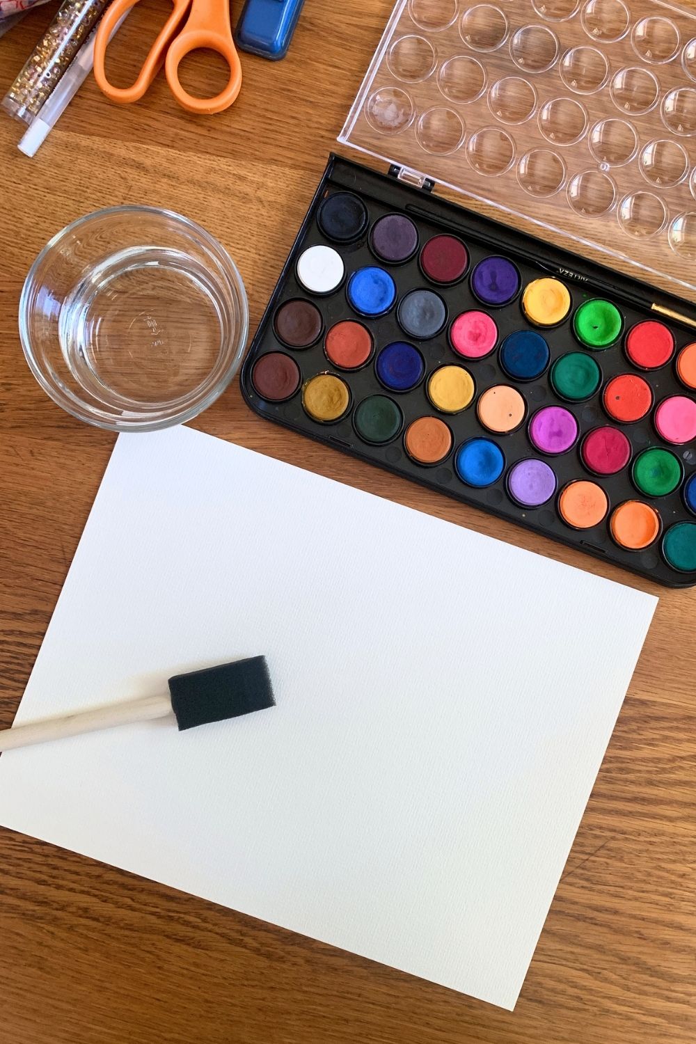 A sponge brush adding clear water to white watercolor paper.