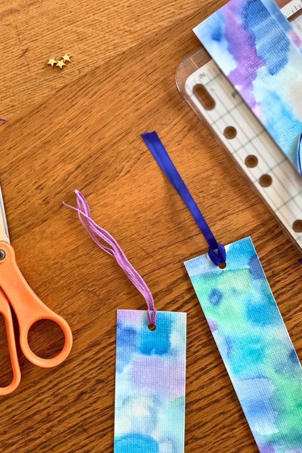 Purple embroidery thread and blue ribbons looped through a hole in the top of the bookmarks.
